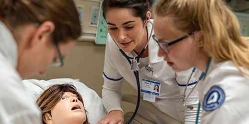 Three female nursing students practice on a mannequin in the health simulation lab.