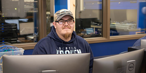 A male developer works in front of monitors at his desk.