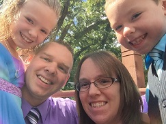 Drew Batterson smiles for photo with wife and two children surrounding him.